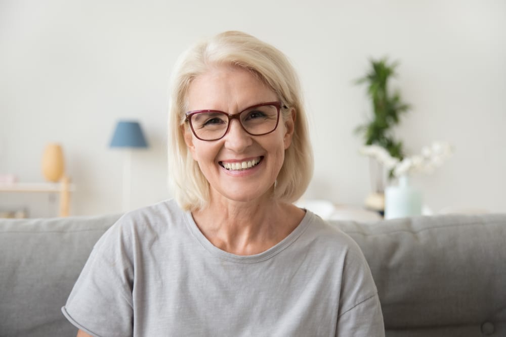 A mature woman with purple framed glasses smiles while posing for a picture