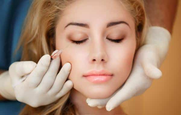 doctor in gloves injecting dermal filler into face of female patient