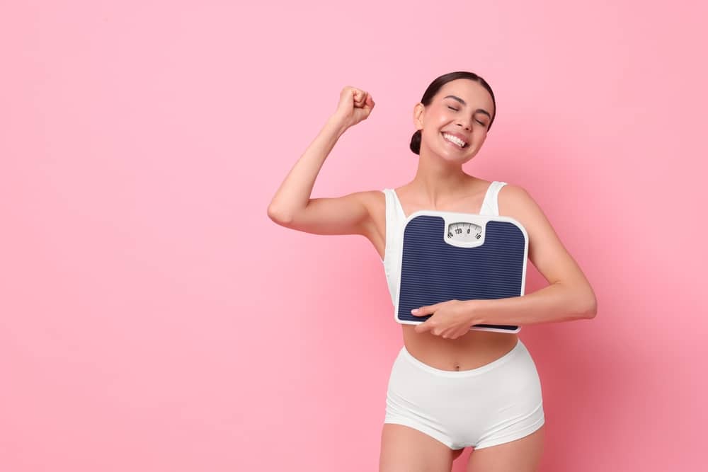 A woman holding a scale and smiling after seeing results from medical weight loss in Knoxville