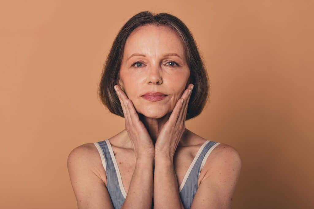 Older woman holding her face in her hands, looking happy after getting a mini facelift to refresh her appearance