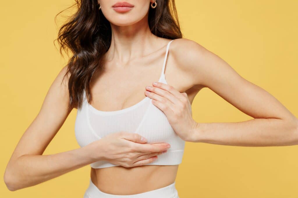 Close up of a young woman holding up her breast, showing her need for a breast lift